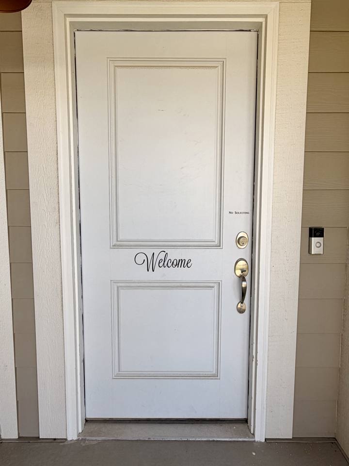White front door before painting, with a worn, scuffed finish and dark marks along the frame edges